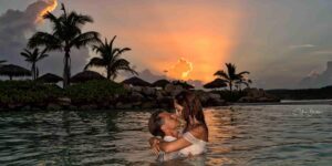 Couple kissing in the water at sunset with palm trees in the background