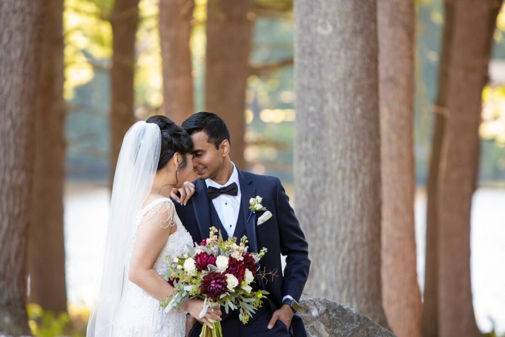 Bride and groom sharing an intimate moment outdoors, with the bride holding a bouquet of flowers and trees in the background