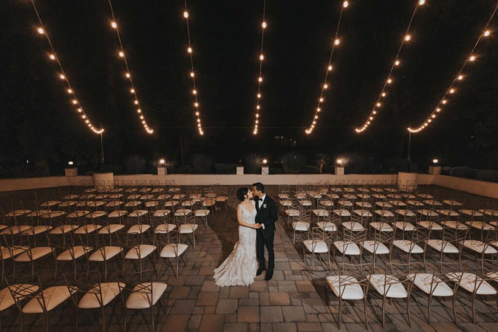 Bride and groom standing together at night under string lights in an empty outdoor ceremony area at The Estate at Farrington Lake, East Brunswick, NJ