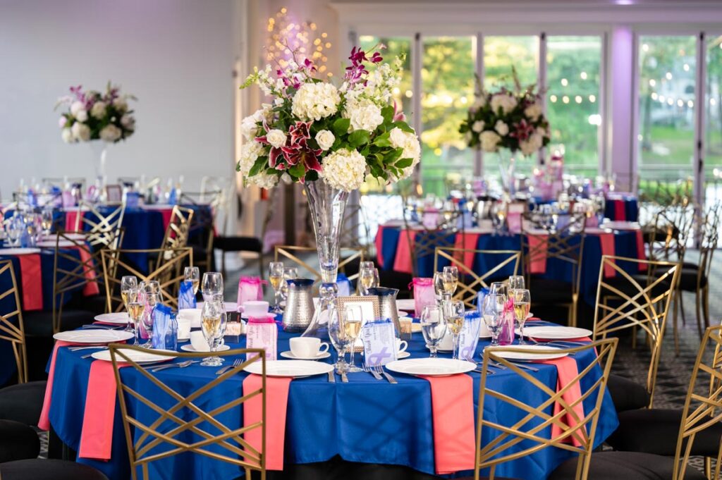 Elegant reception table settings featuring blue and pink tablecloths adorned with floral centerpieces and glassware, ready for guests at The Estate at Farrington Lake, East Brunswick, NJ