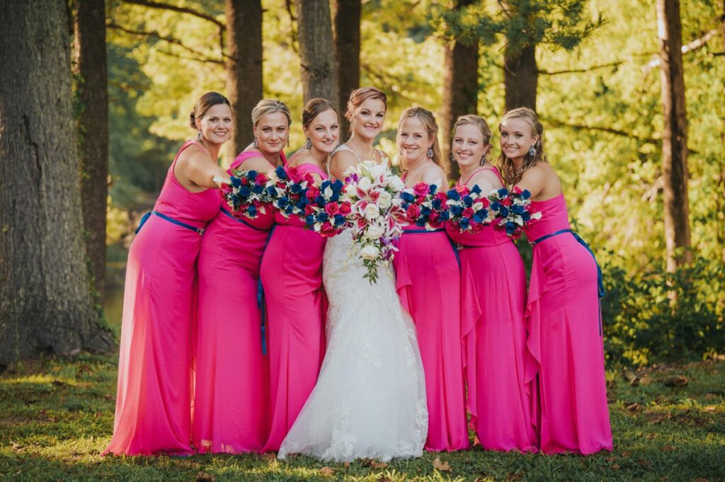 Bride surrounded by her bridesmaids, all smiling and posing together in a sunny outdoor setting at The Estate at Farrington Lake, East Brunswick, NJ