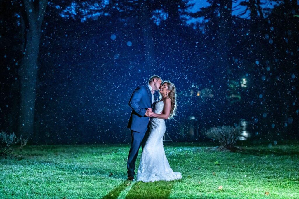groon and bride dancing at night under a tree illuminated by lights in a park