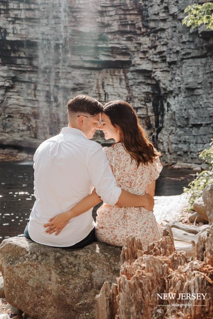 Engaged couple sitting on rocks by the water