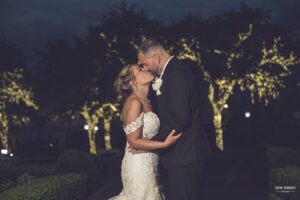 Bride and groom kissing at night with lit trees behind them