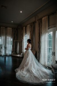 Bride in a flowing gown standing by a large window in an elegant room
