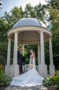 Bride and groom standing under a gazebo in a garden setting