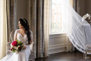 Bride sitting by a window, holding a bouquet, and smiling as she looks outside