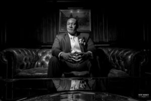Groom seated on a leather sofa in a dark, elegant room, looking thoughtful