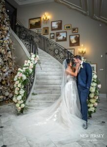 Bride and groom sharing a tender moment at the base of an elegantly decorated staircase with floral arrangements
