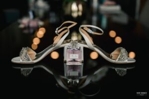 Bridal heels arranged around a perfume bottle, reflected on a glossy surface