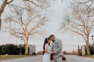 Bride and groom sharing a kiss outdoors under trees wrapped in string lights