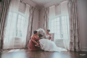 Bride sitting in an elegant room while a bridesmaid helps adjust her shoe