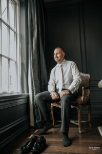 Groom sitting by a window, smiling while getting ready
