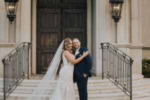 Bride and groom smiling and embracing on the steps in front of a church